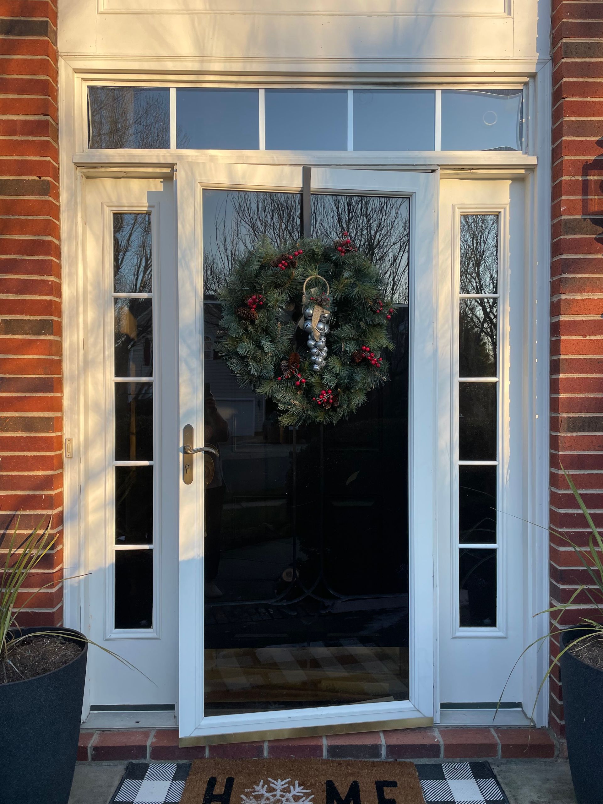 White front door with a wreath, flanked by sidelights, set in a red brick wall. The door is slightly ajar, and a