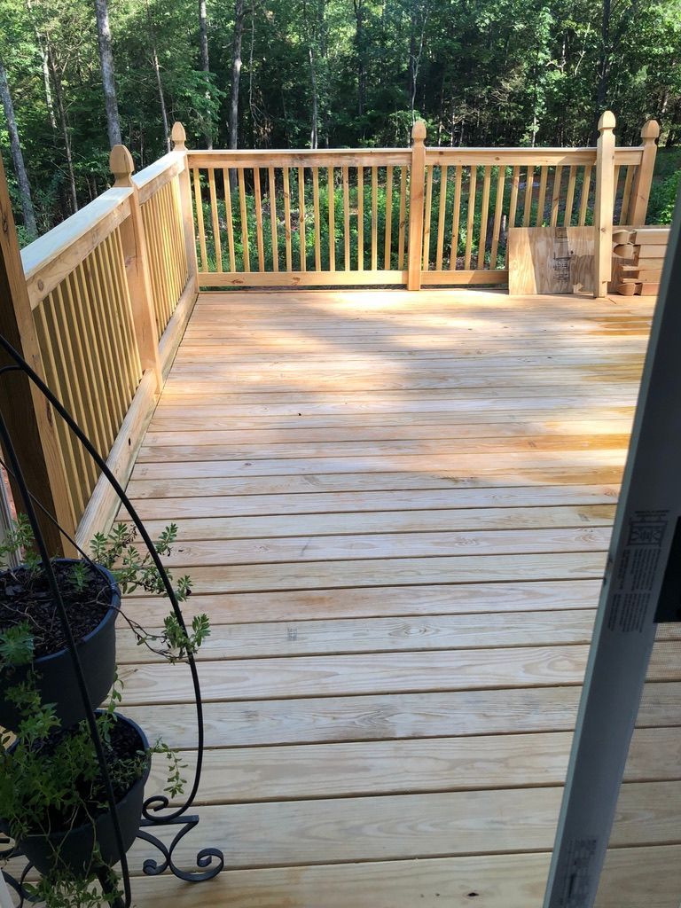 Wooden deck with railing in a forest setting, plants in pots on the side.