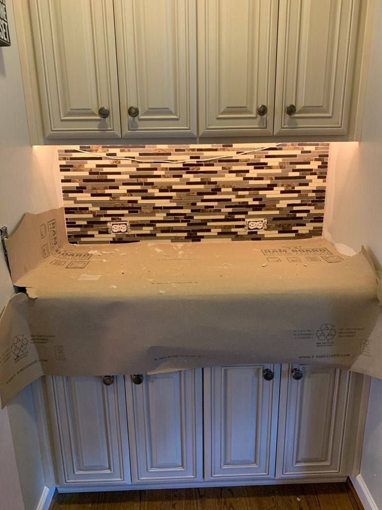 Kitchen cabinets with a patterned tile backsplash and under-cabinet lighting. Brown paper protects the countertop.