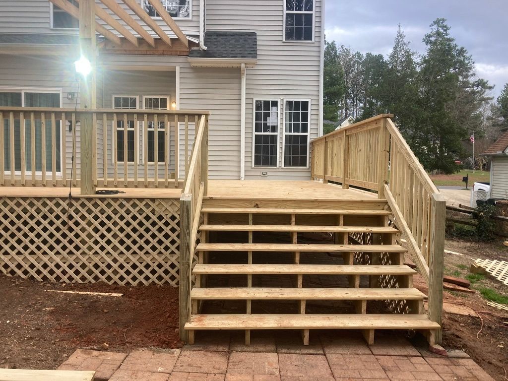 Wooden deck with stairs leading to a house with light siding and windows. A ramp is built to the right.