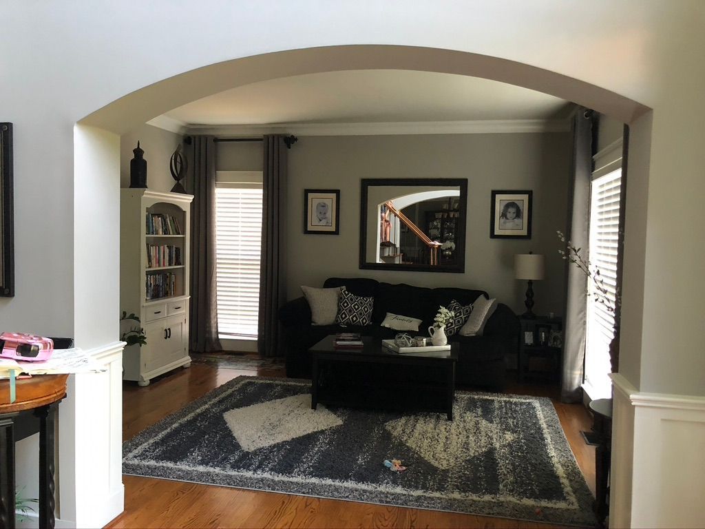 Living room with gray walls, dark couch, and rug under an arched entryway. A white bookcase and framed artwork are also visible.