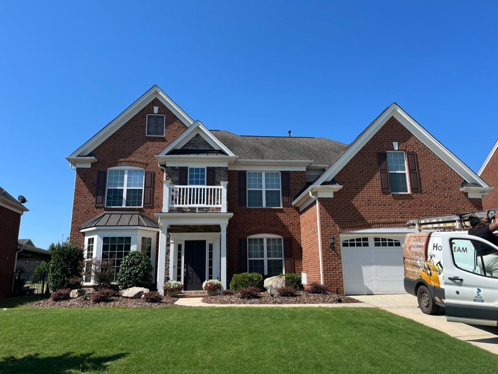 Two-story brick house with white trim, dark blue front door, and a white garage door, set against a bright blue sky.