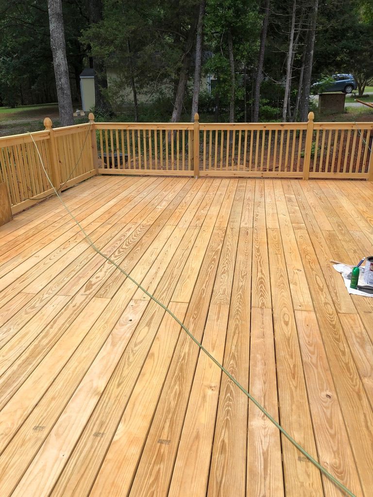 Wooden deck with railing in a wooded outdoor setting, freshly stained.