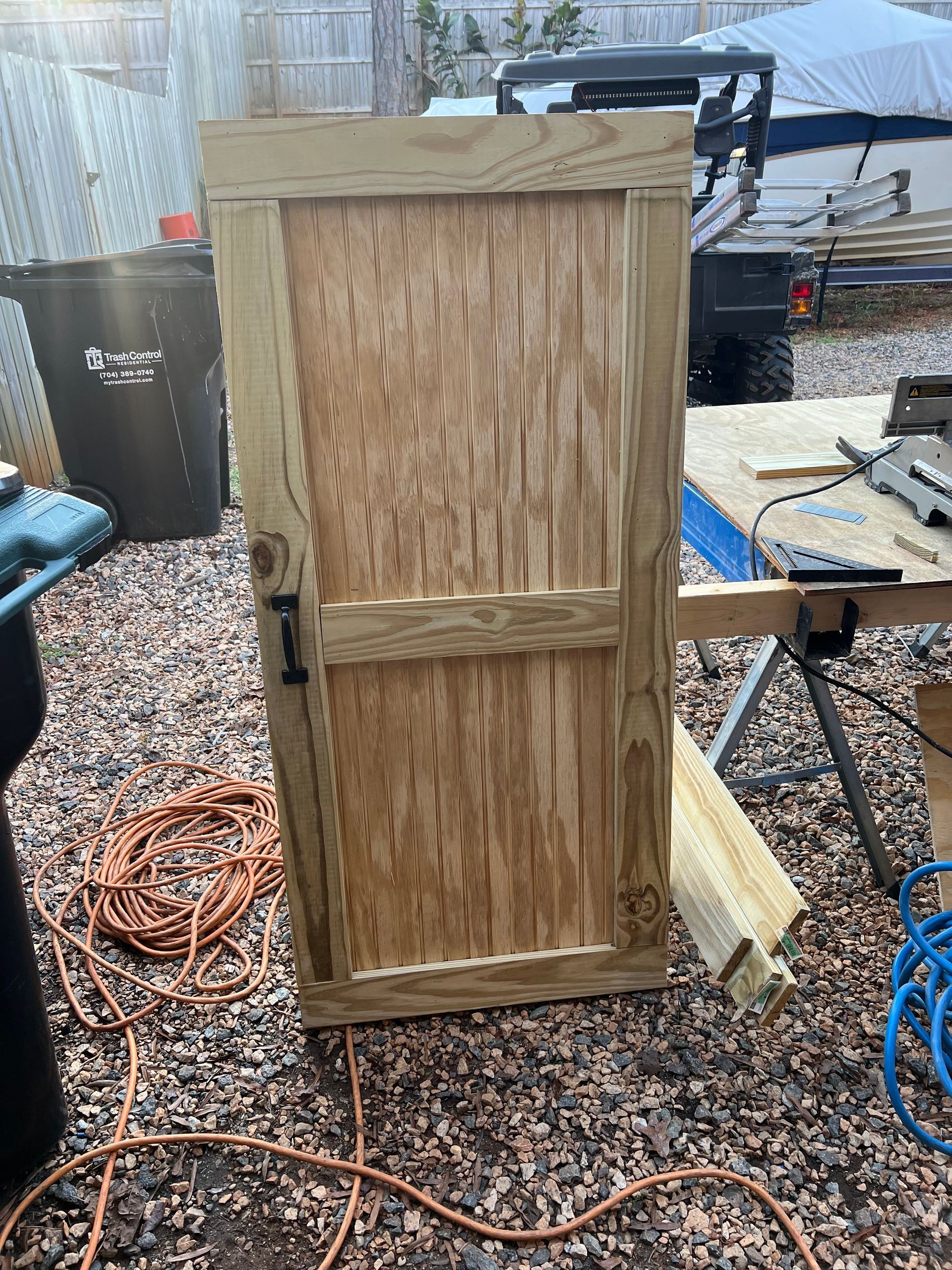 Wooden gate under construction, outdoors. Features a rustic design with a black latch and frame.