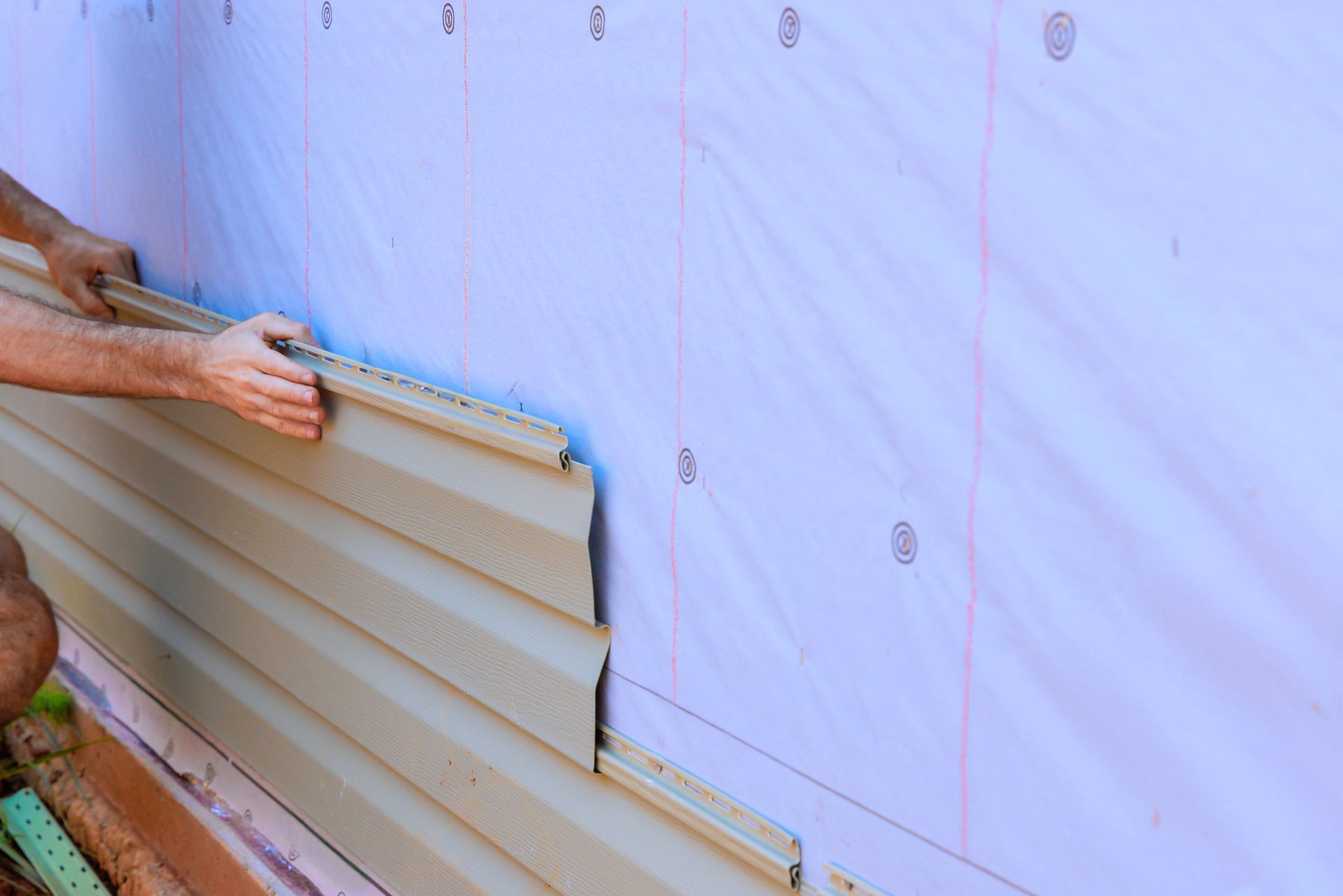 Person installing light brown vinyl siding on a building with white insulation.