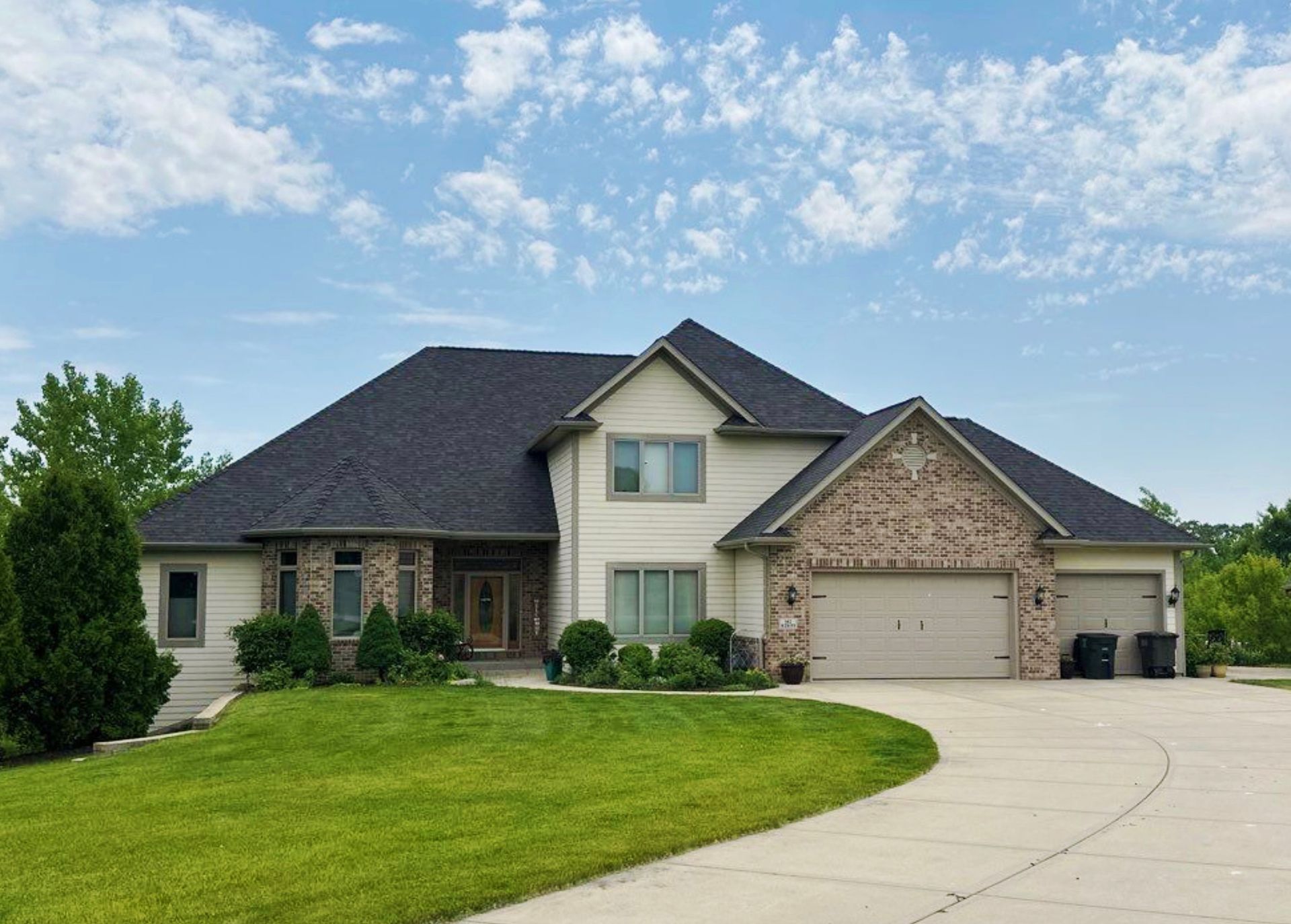 Two-story house with a green lawn, curved driveway, and blue sky.
