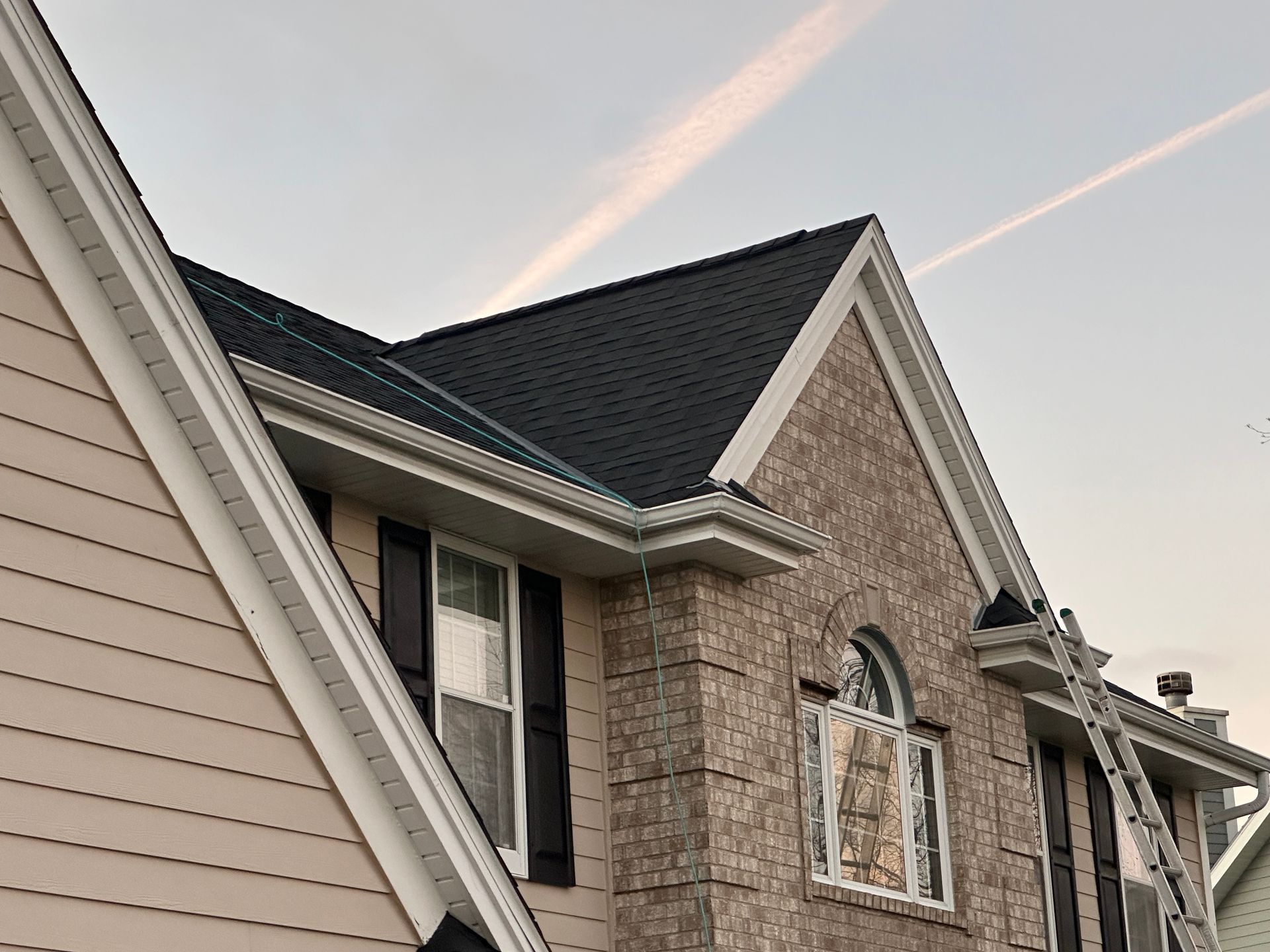 House exterior with a brick and siding facade, new dark roof, and a ladder.