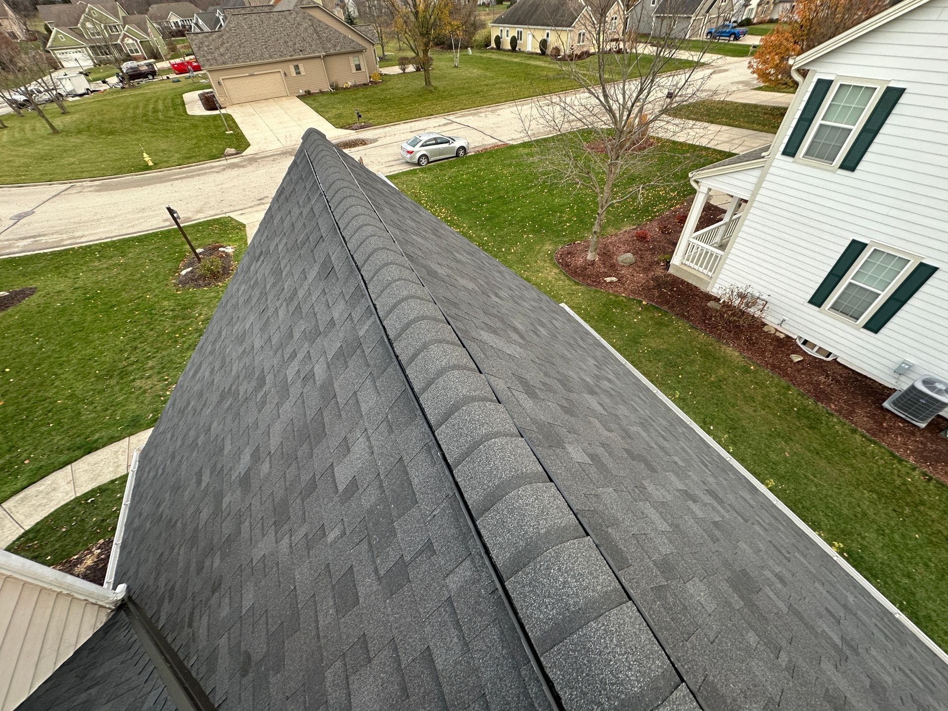 Dark gray shingled roof of a house in a suburban setting, viewed from above.