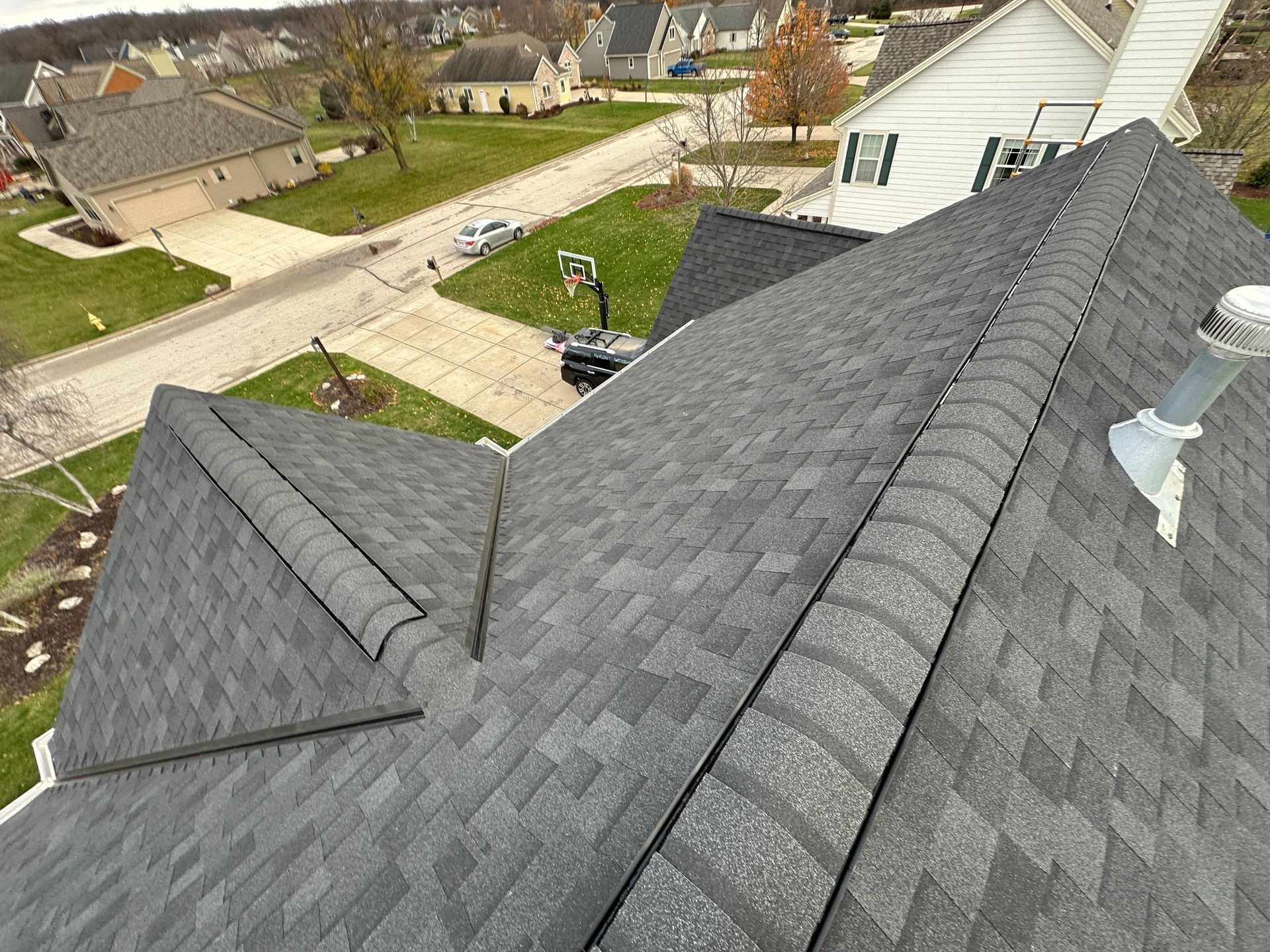 Gray asphalt shingle roof on a house, viewed from above, with a neighborhood in the background.