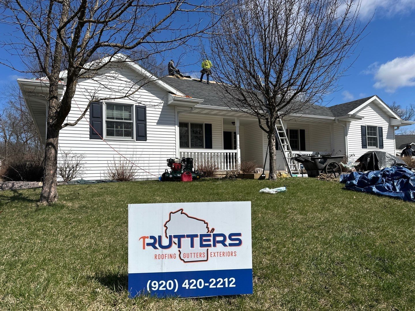 House with roofers. White house, green lawn, ladder, blue tarp, Rutters sign.