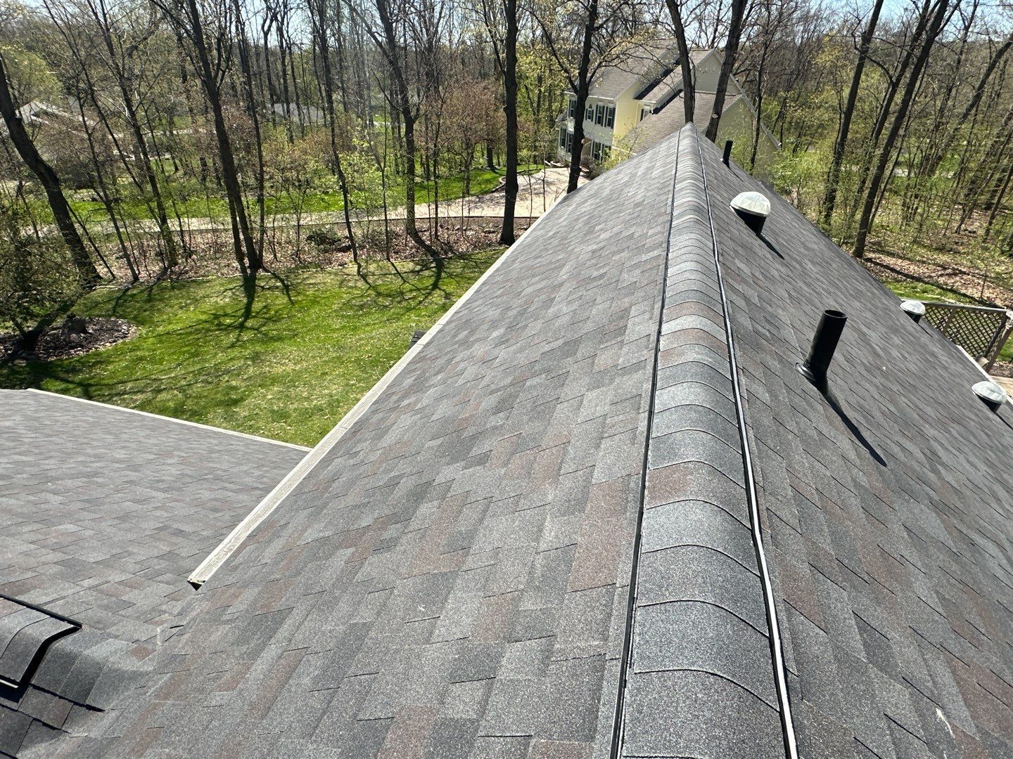 Overhead view of a shingled roof with a dark brown and grey color scheme. A vent pipe is visible.