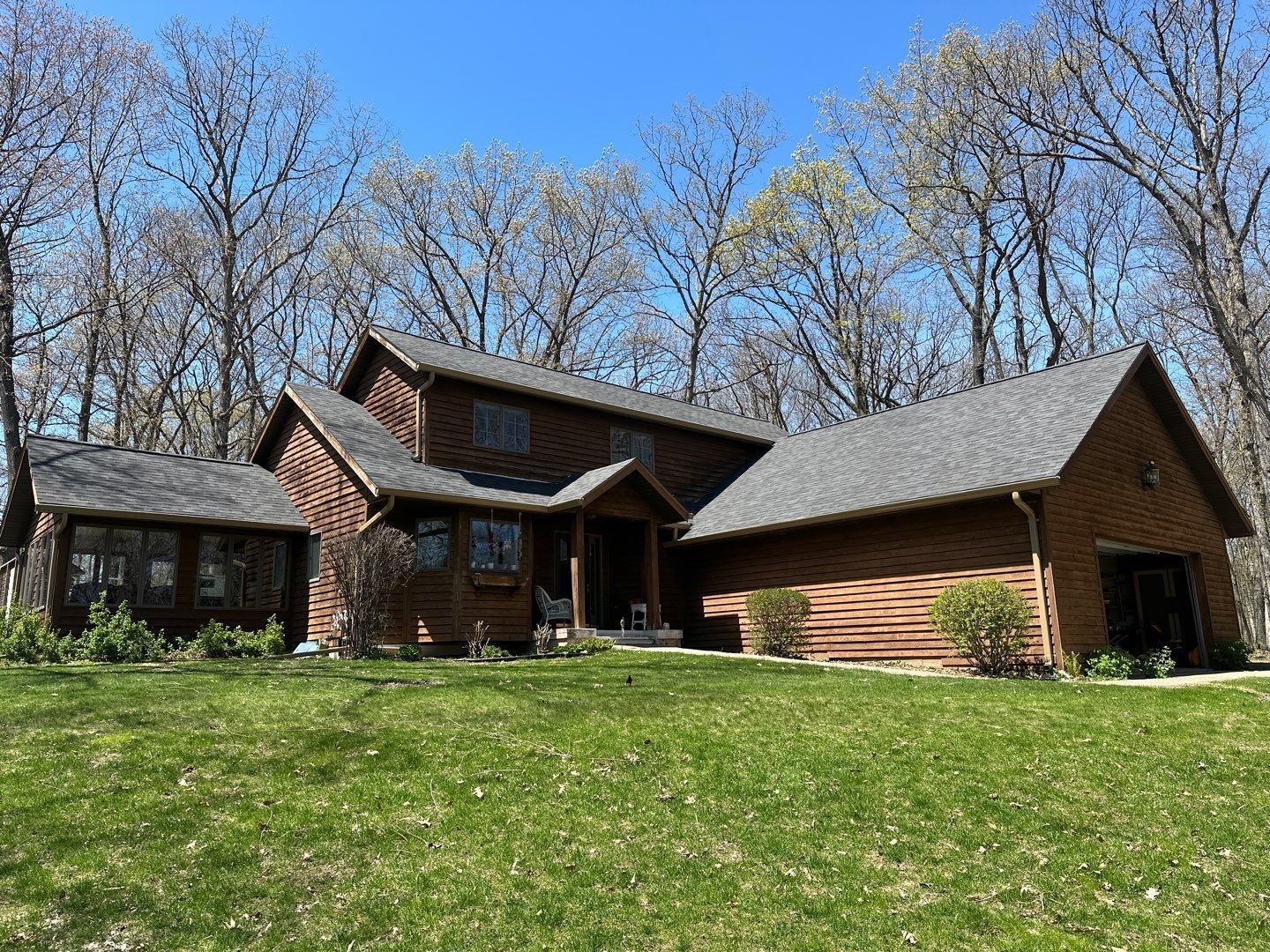 Brown house with a gable roof, surrounded by trees and a green lawn under a blue sky.
