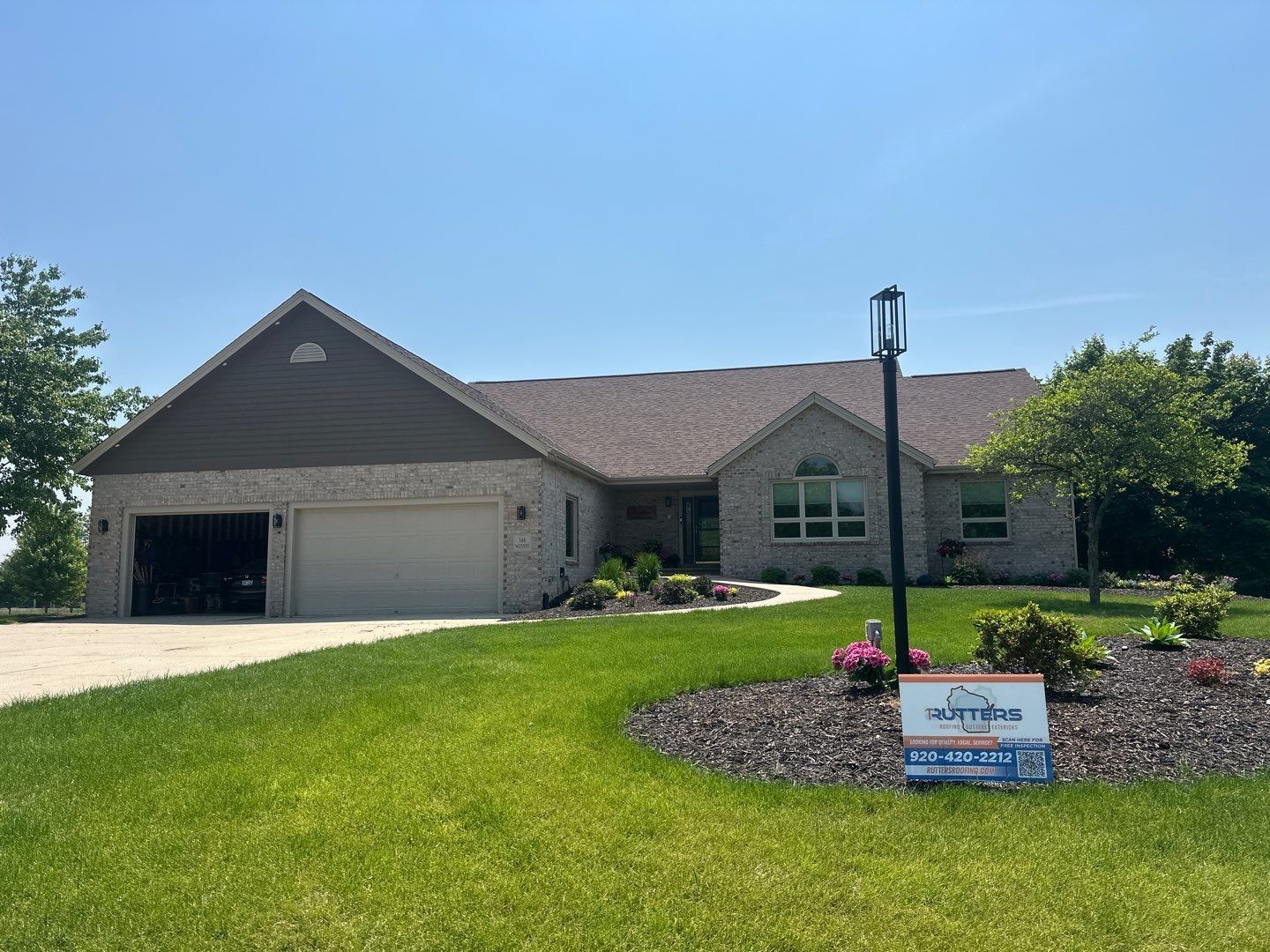 Brick house with attached garage, landscaped lawn, and a sign in the yard.