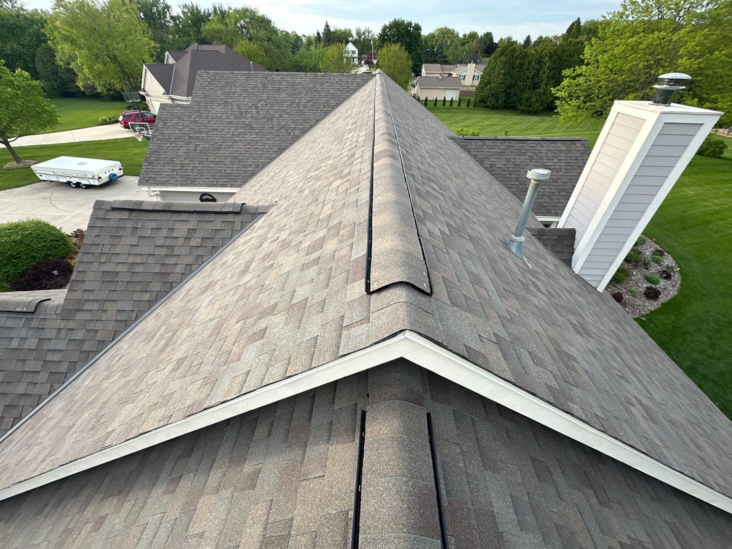 Overhead view of a gray asphalt shingle roof with a chimney and surrounding trees.