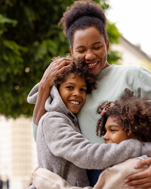 Three people hugging outdoors, smiling warmly in a close family embrace.