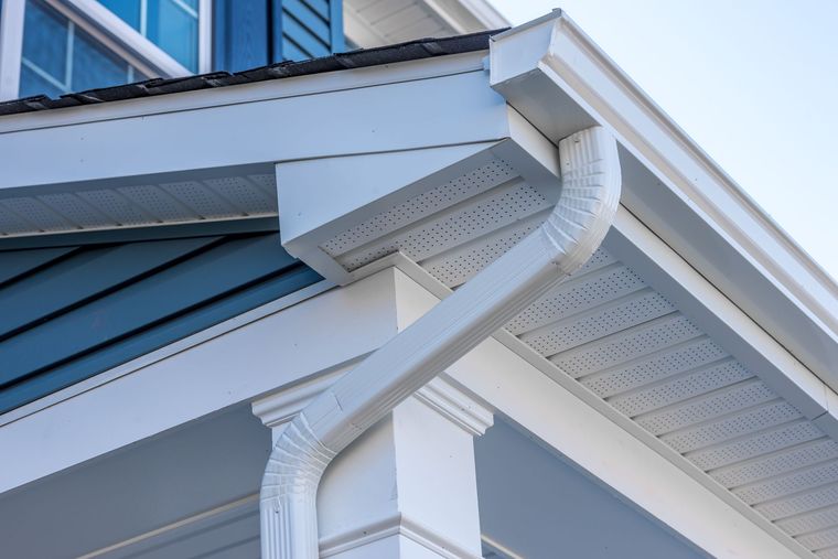 White house eave with curved downspout and blue siding detail White house eave with curved downspout and blue siding detail