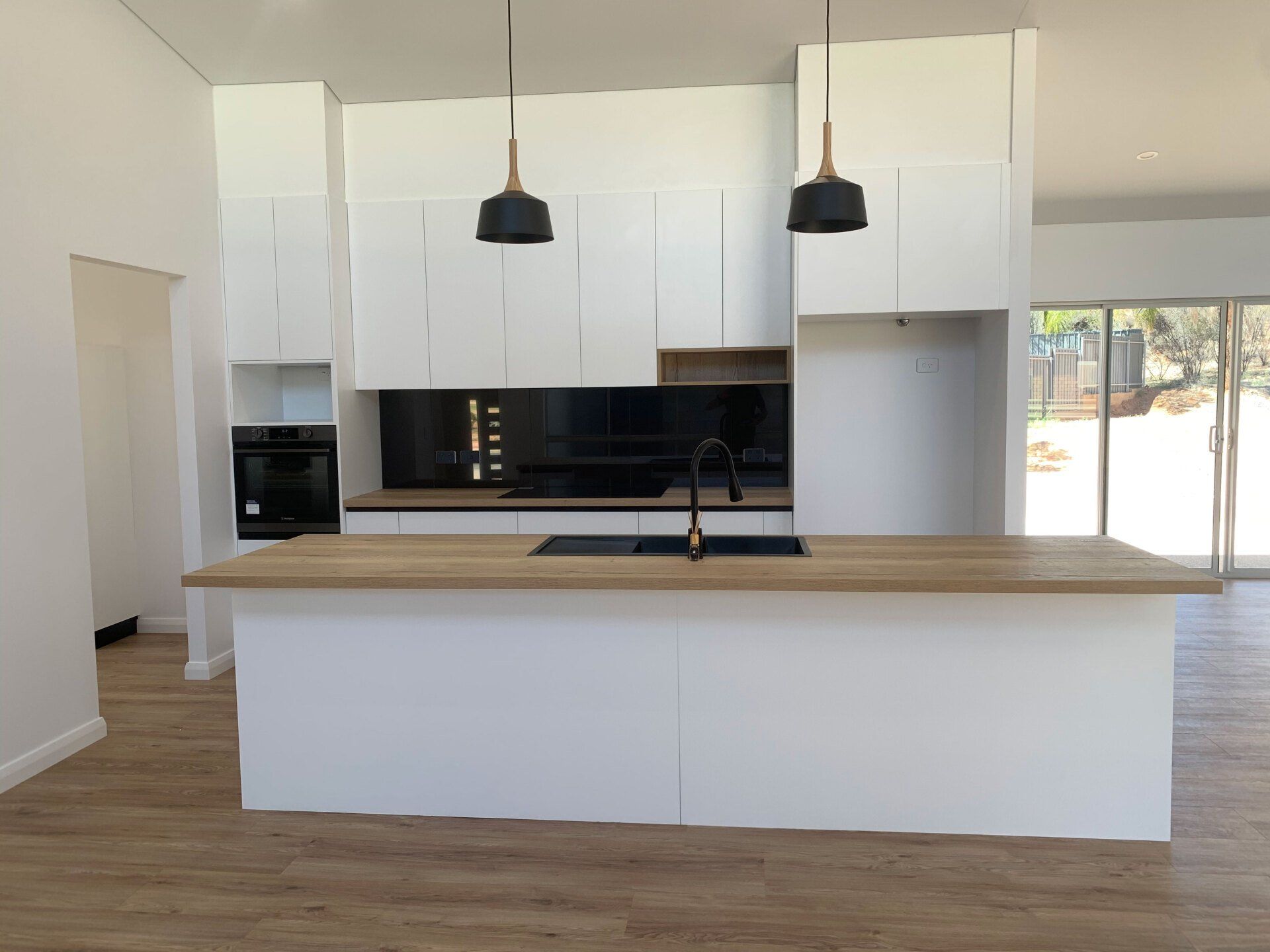 Modern white kitchen with island and black accents, wood countertops and pendant lights.