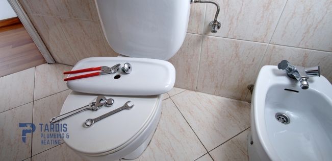 A toilet and bidet in a bathroom with tools on the seat.
