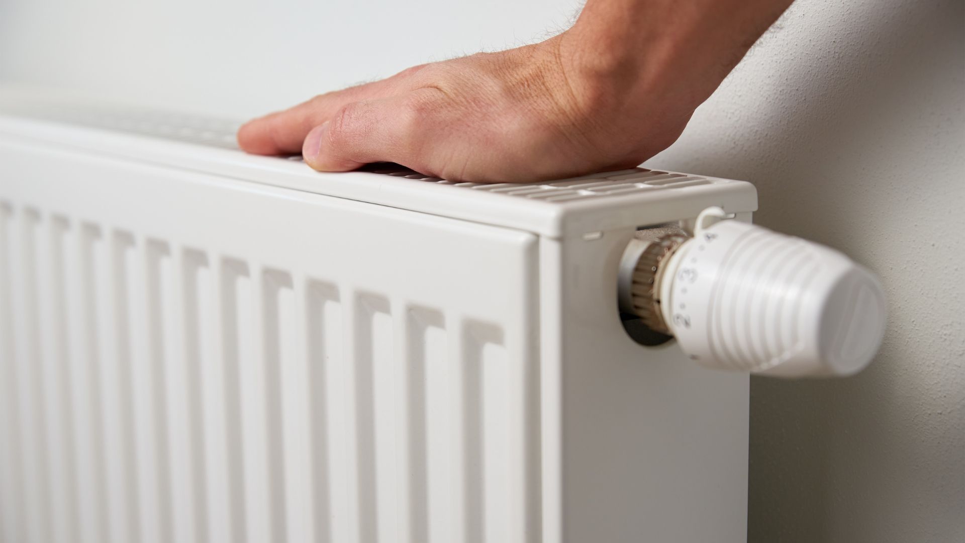 A person is touching a radiator with their hand.