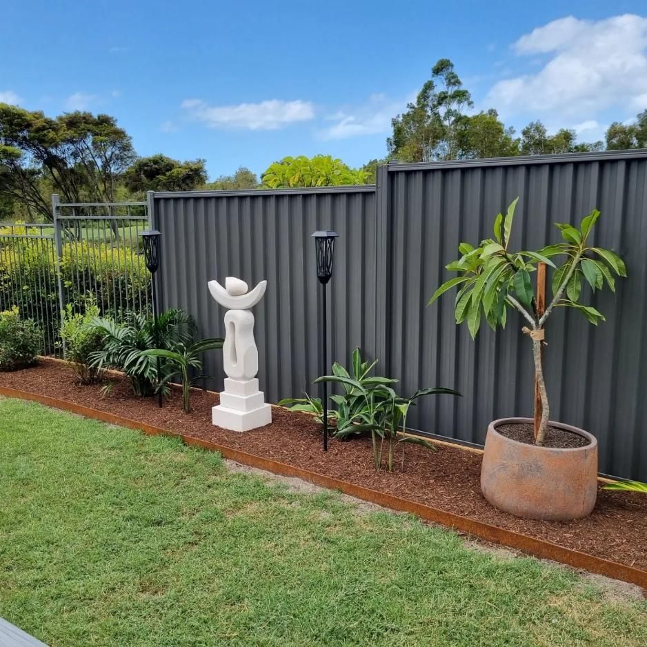 A Garden With A Fence, Potted Plants, A Statue And A Torch — All Aspects Landscaping In Coolum Beach, QLD