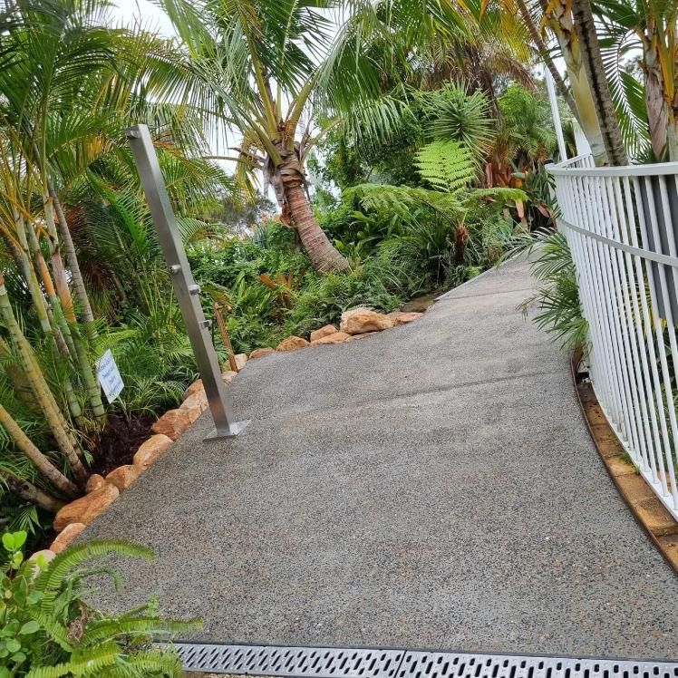 A Concrete Walkway Surrounded By Palm Trees And A White Fence — All Aspects Landscaping In Peregian Beach, QLD