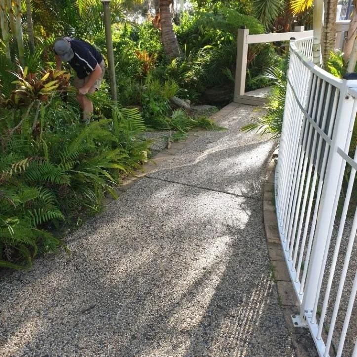 A Man Standing On A Sidewalk Next To A White Fence — All Aspects Landscaping In Peregian Beach, QLD