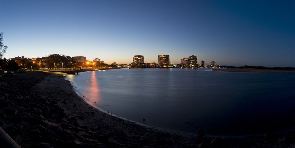 A City Skyline Is Visible Over A Body Of Water At Night — All Aspects Landscaping In Maroochy River, QLD