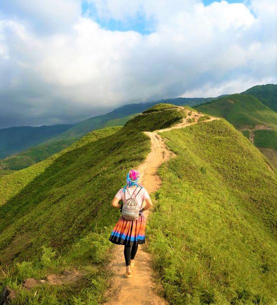 A woman is walking down a dirt path on top of a hill.