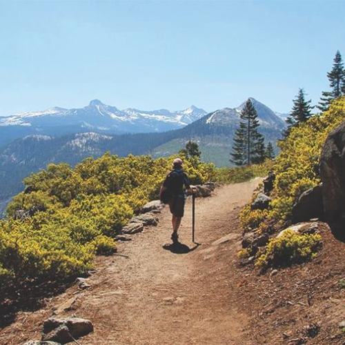 A man is walking down a dirt path in the mountains.