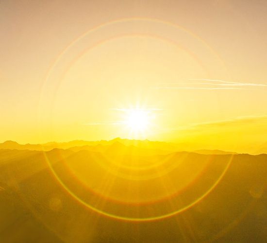 The sun is shining brightly over the mountains at sunset.