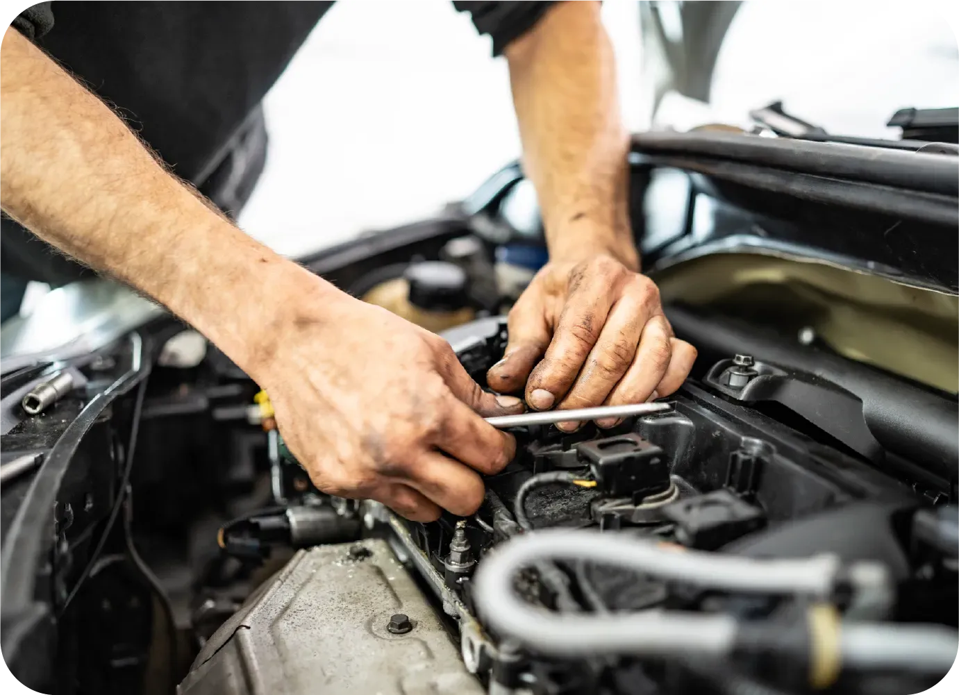 A mechanic uses a tool to work on the engine of a vehicle in an auto repair shop.