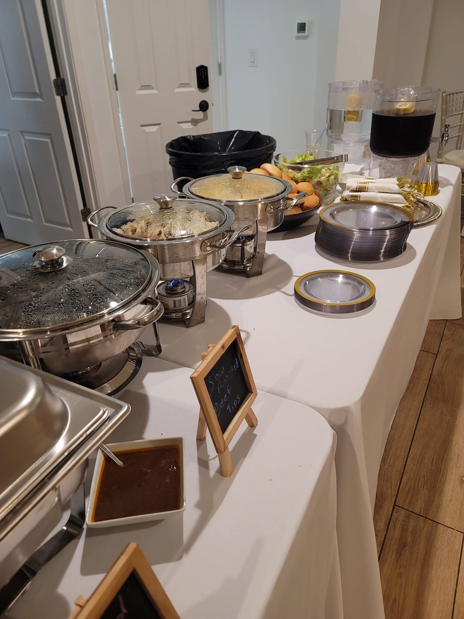 Buffet table with chafing dishes, salads, bread, and desserts set up in a hallway