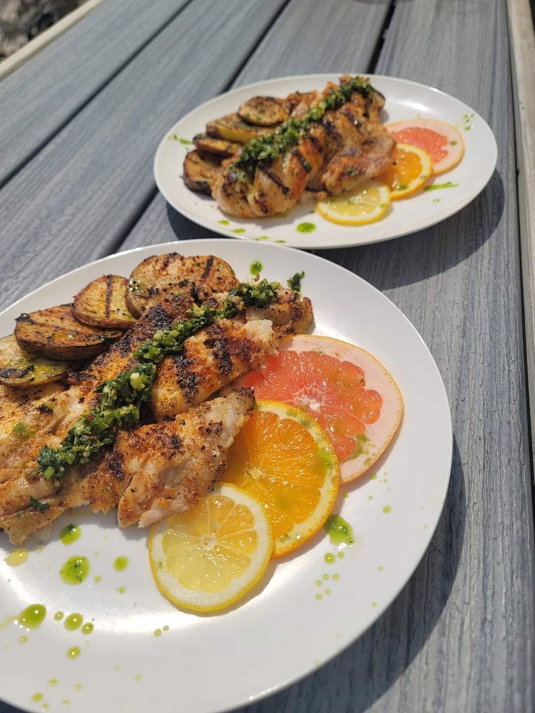 Plates of grilled chicken with lemon and orange slices on a gray table.