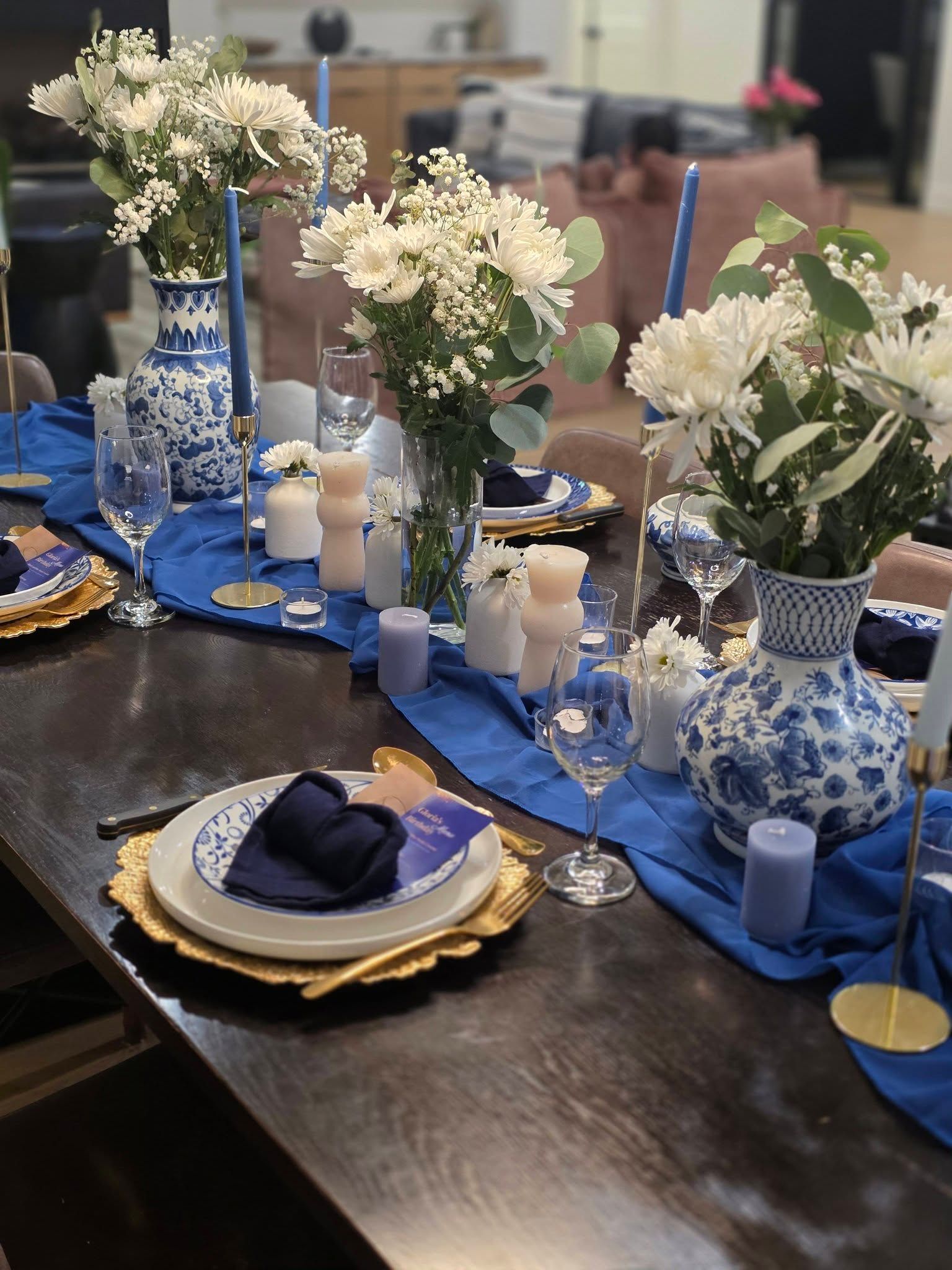 Blue and white floral table setting with candles, plates, and flower arrangements on a dark wooden table