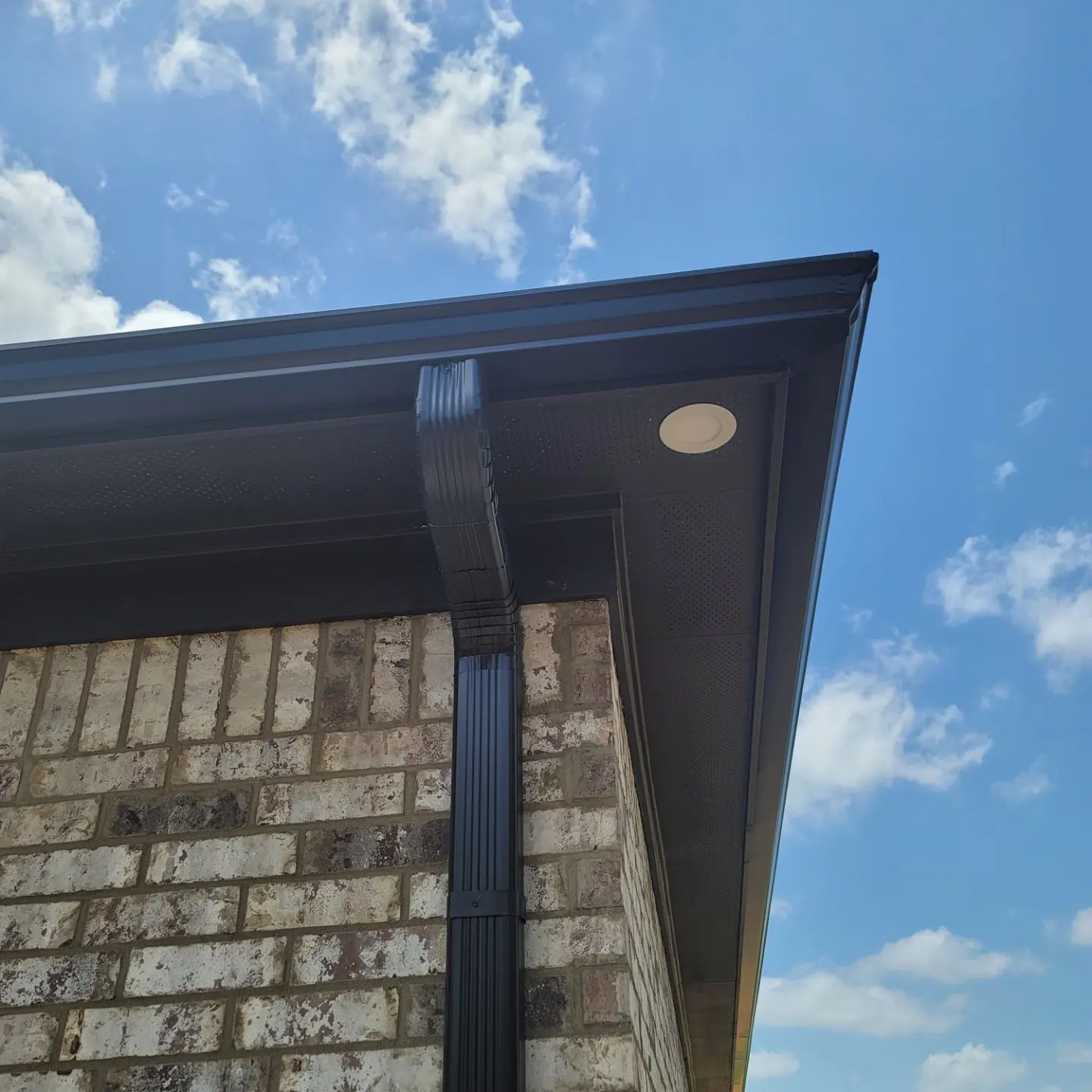 Black rain gutter on brick building, against a blue sky with clouds.