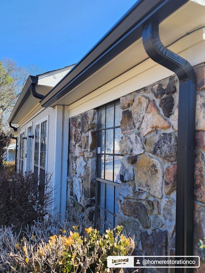 Black gutters on a stone and beige house with a clear blue sky.