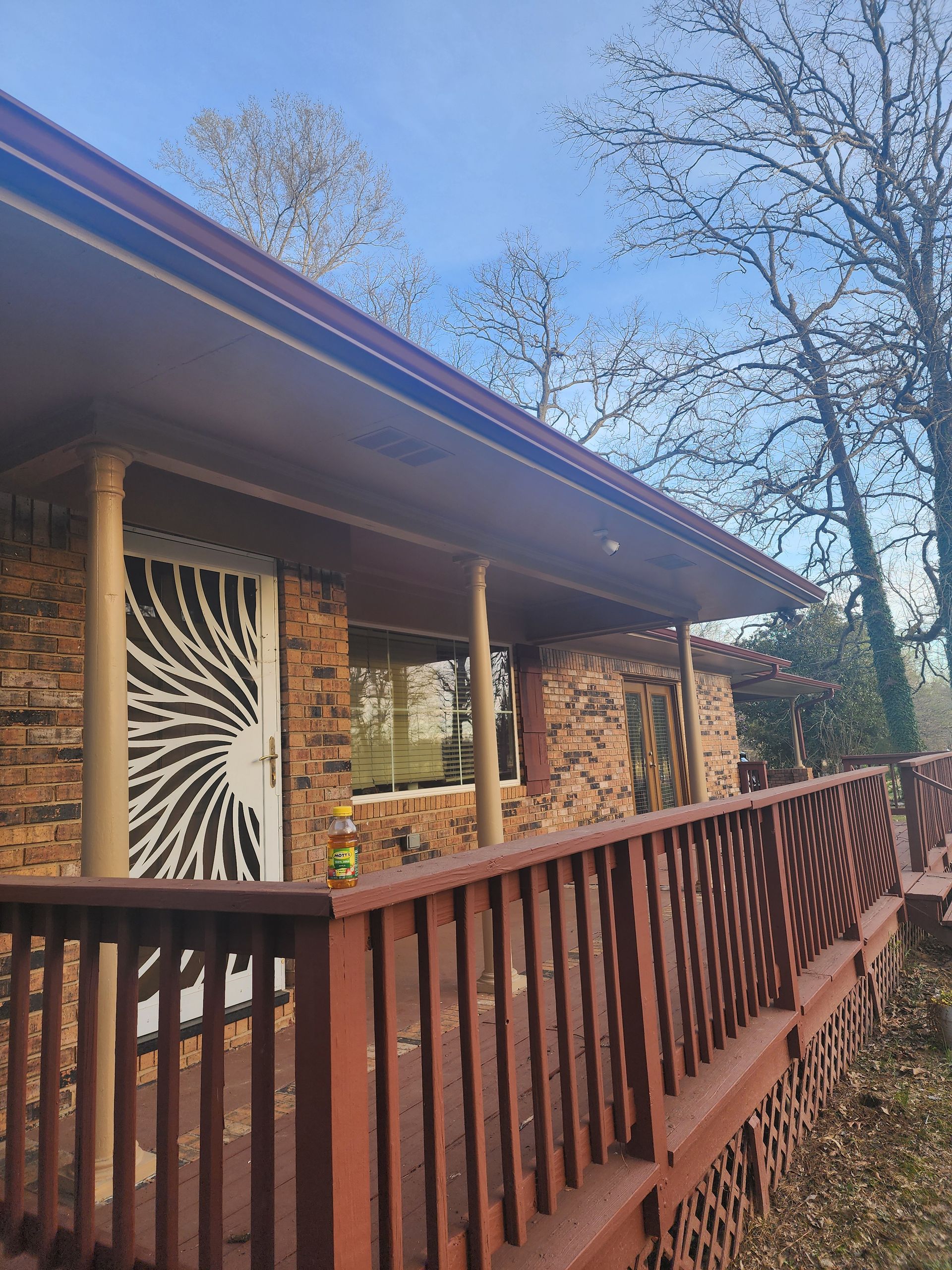 Stone-textured house with a red porch, door with black design, and trees under a blue sky.
