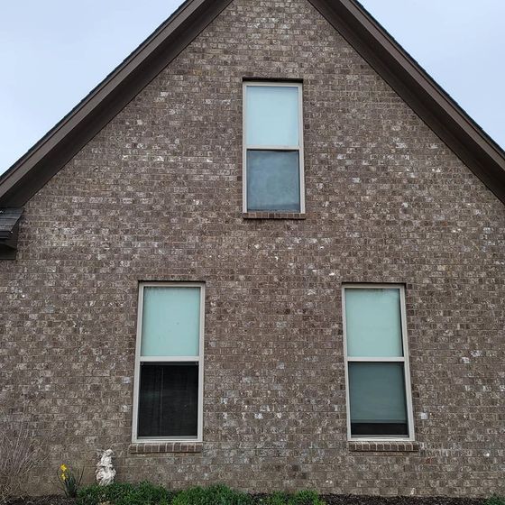 Brick house with three windows; two below and one in the peak; overcast sky.