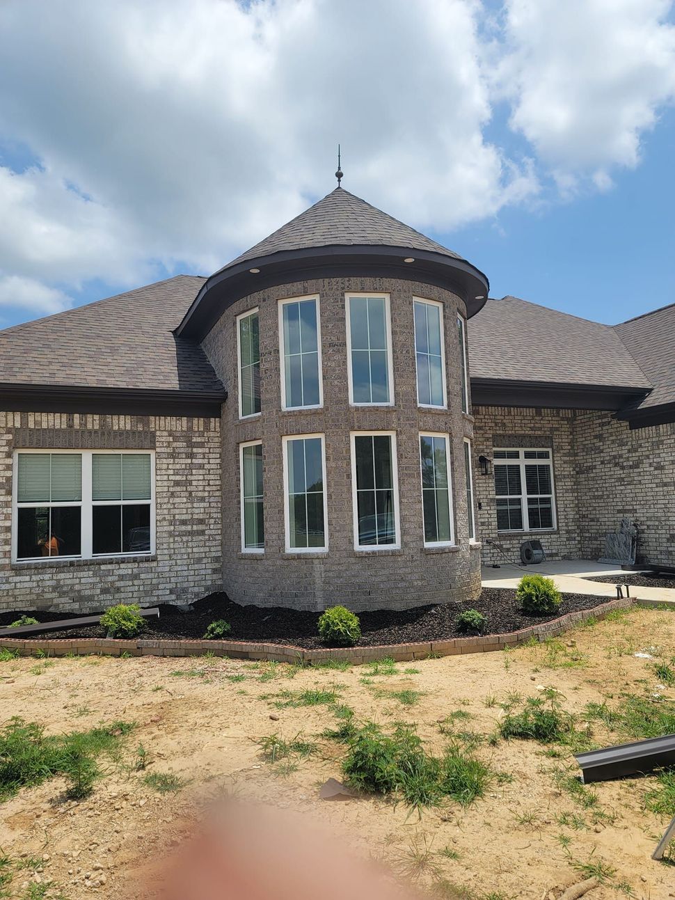 Brick house with a rounded tower of windows, brown roof, and small bushes in front.