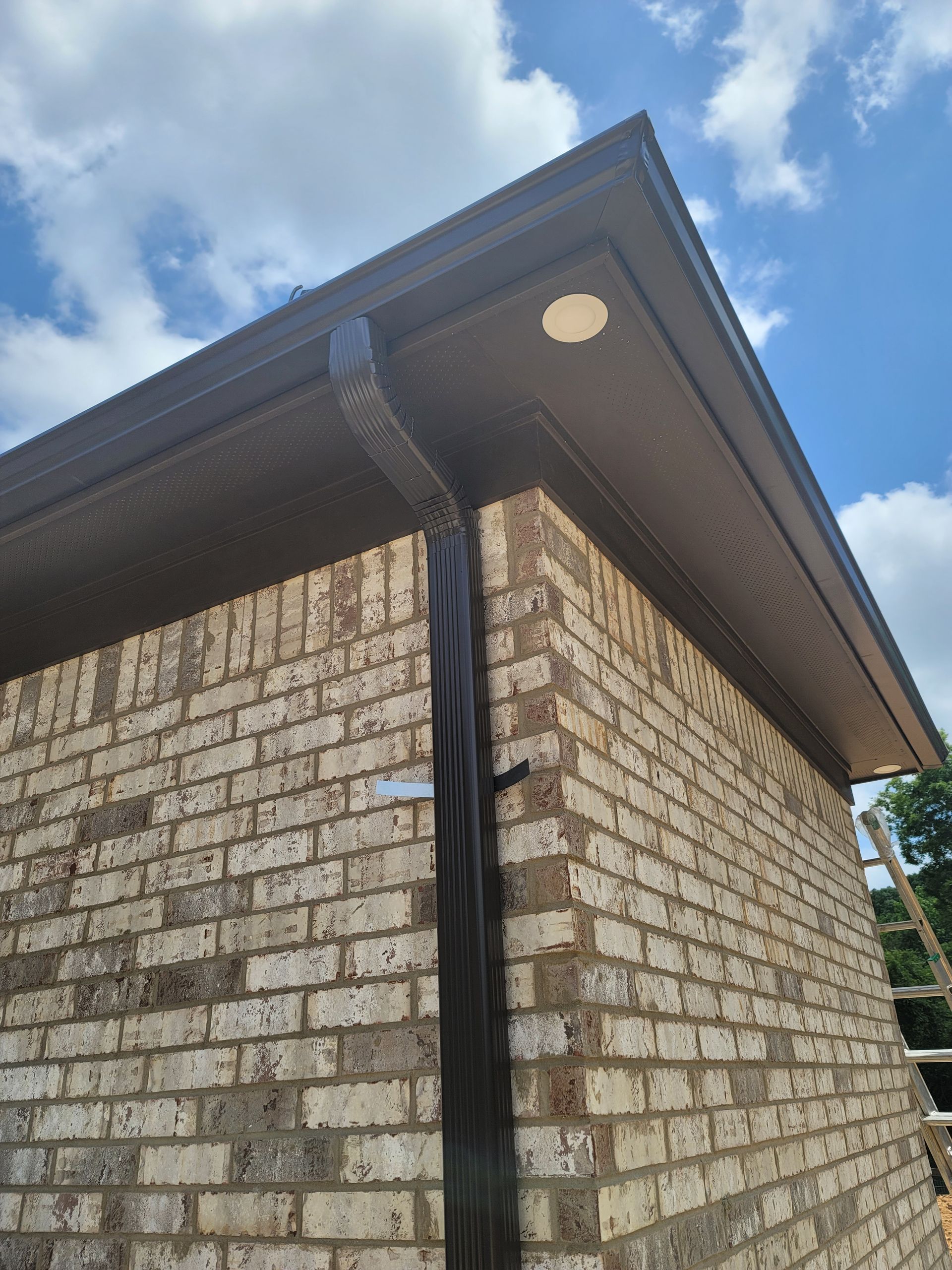 Brown brick building corner with dark gutters and downspout, blue sky.