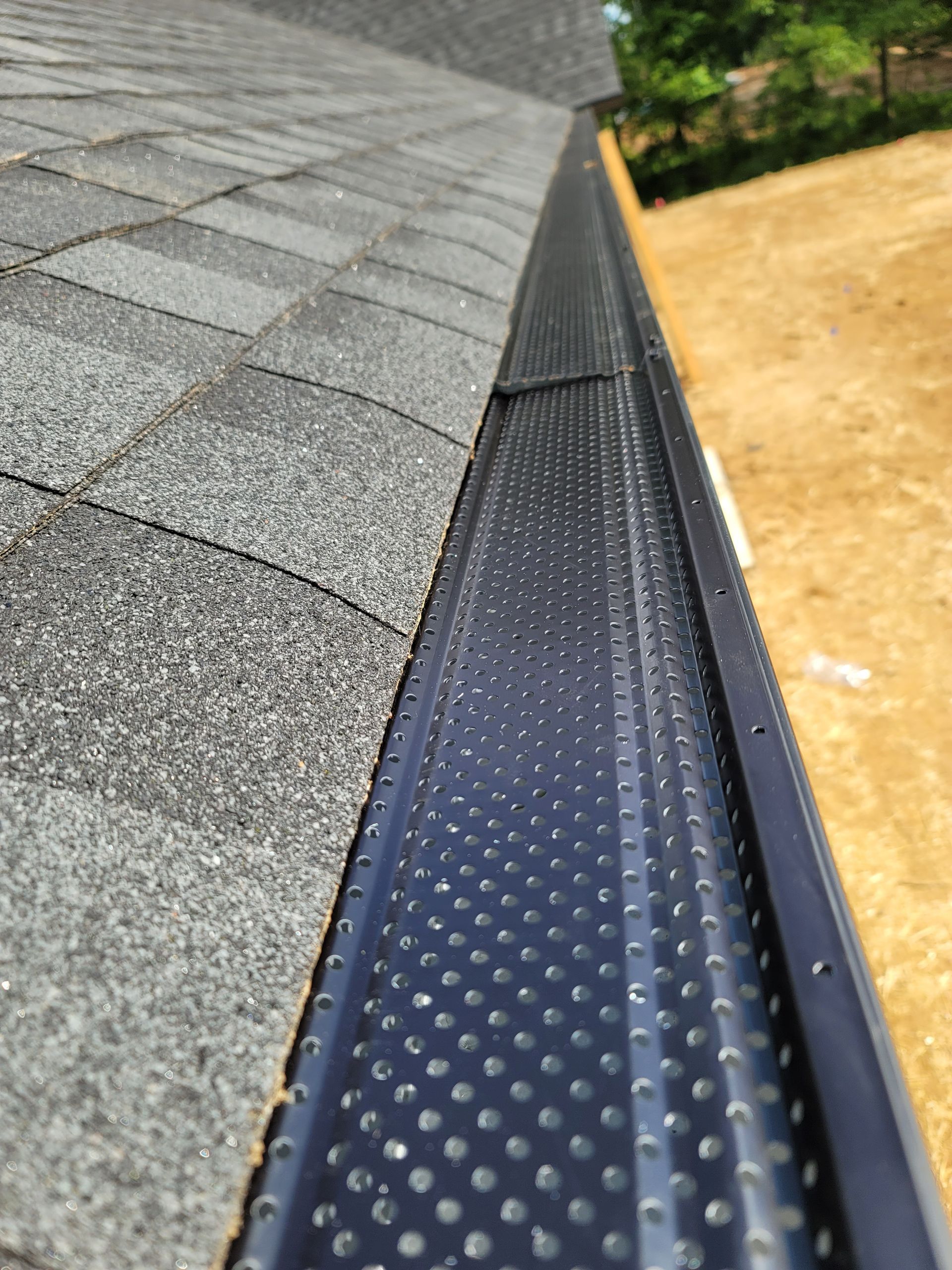 Black gutter guard on a roof with gray shingles, seen from a low angle.