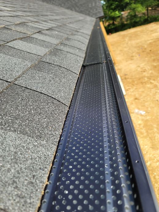 Black gutter guard on a roof with gray shingles, seen from a low angle.