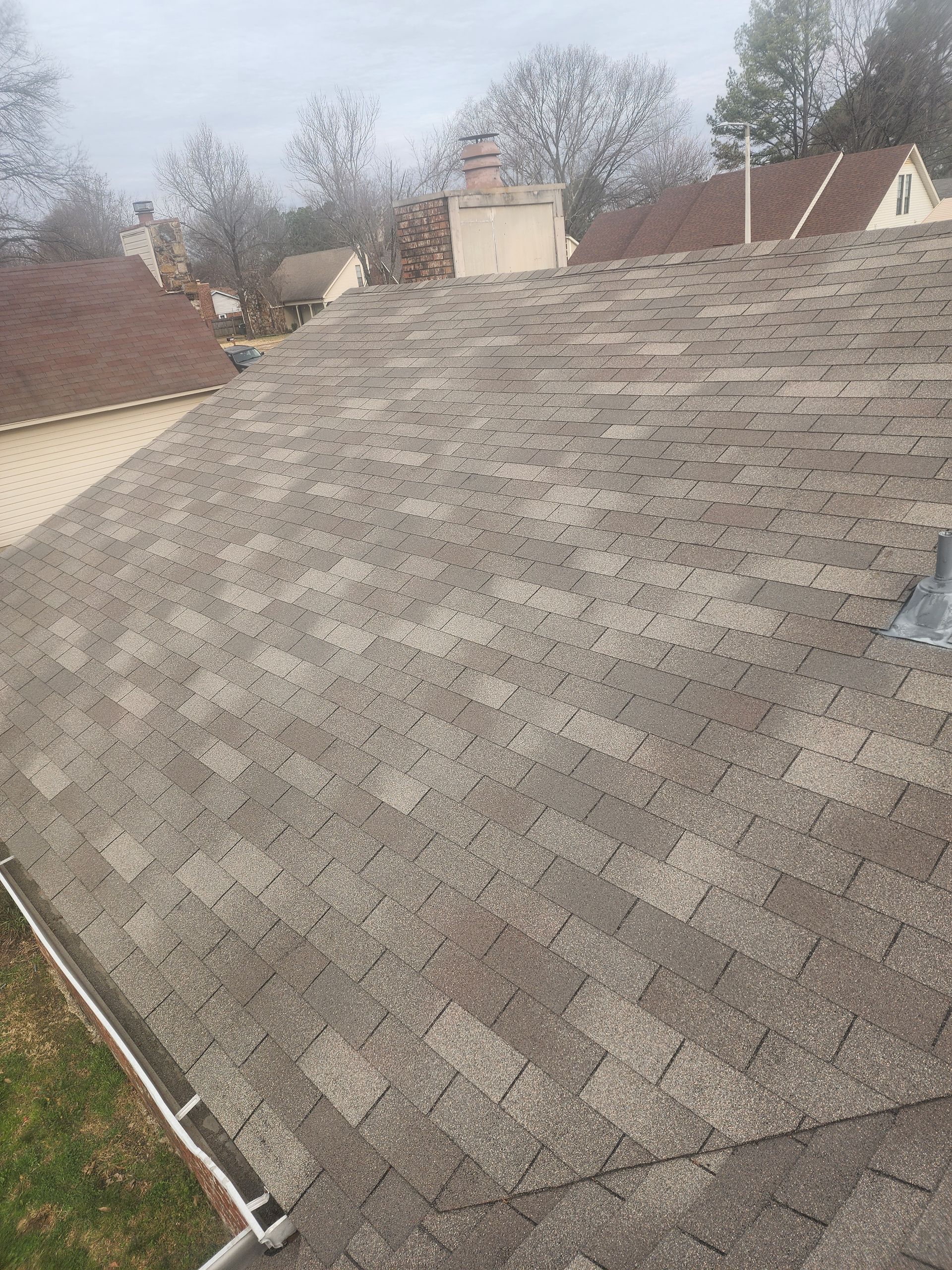 Asphalt shingle roof on a house with a chimney in an overcast setting.