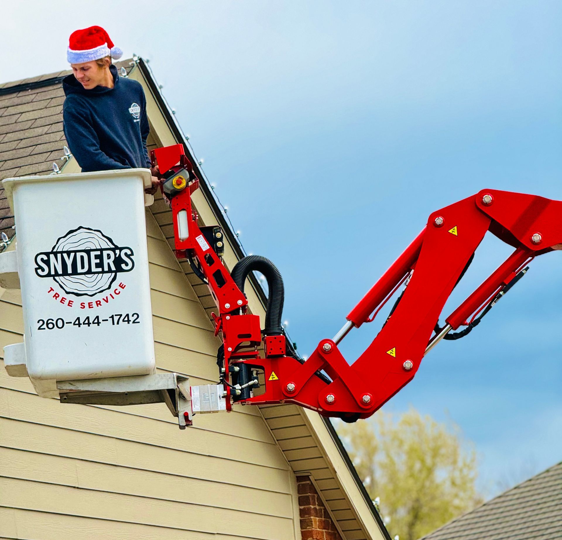 Man in Santa hat uses a lift to install Christmas lights on a house.
