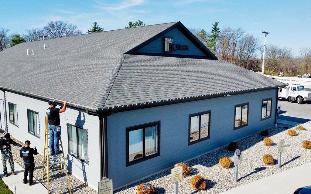 Workers on scaffolding, installing something on a gray building with black trim, rocks, and a sign.