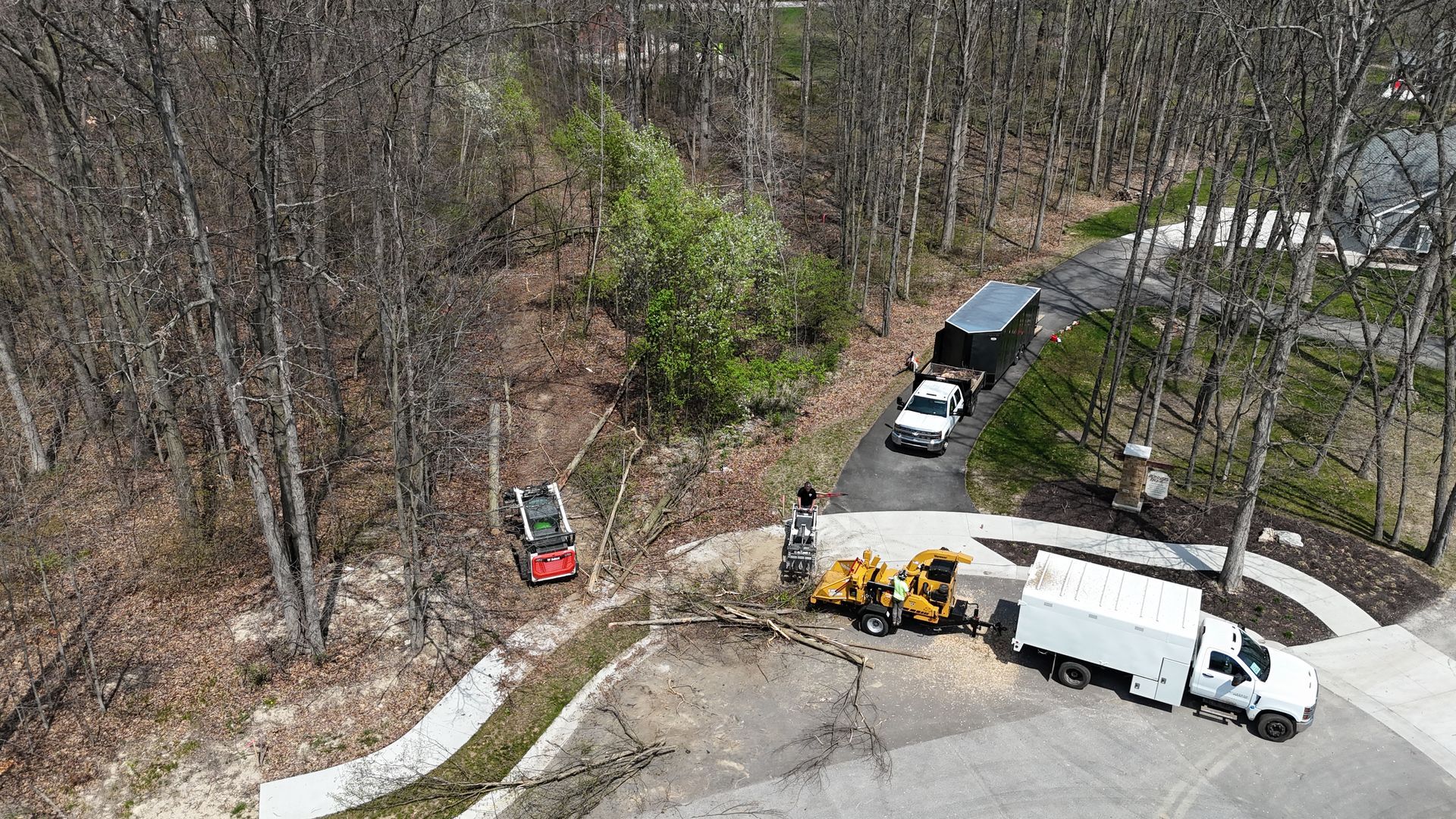Tree removal operation with trucks, chipper, and crew in a wooded residential area.