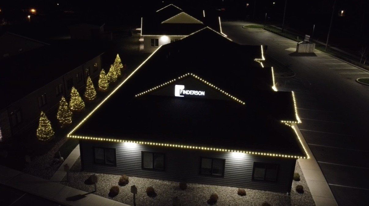 Building at night with roofline and tree lights, illuminated sign, and exterior lights.