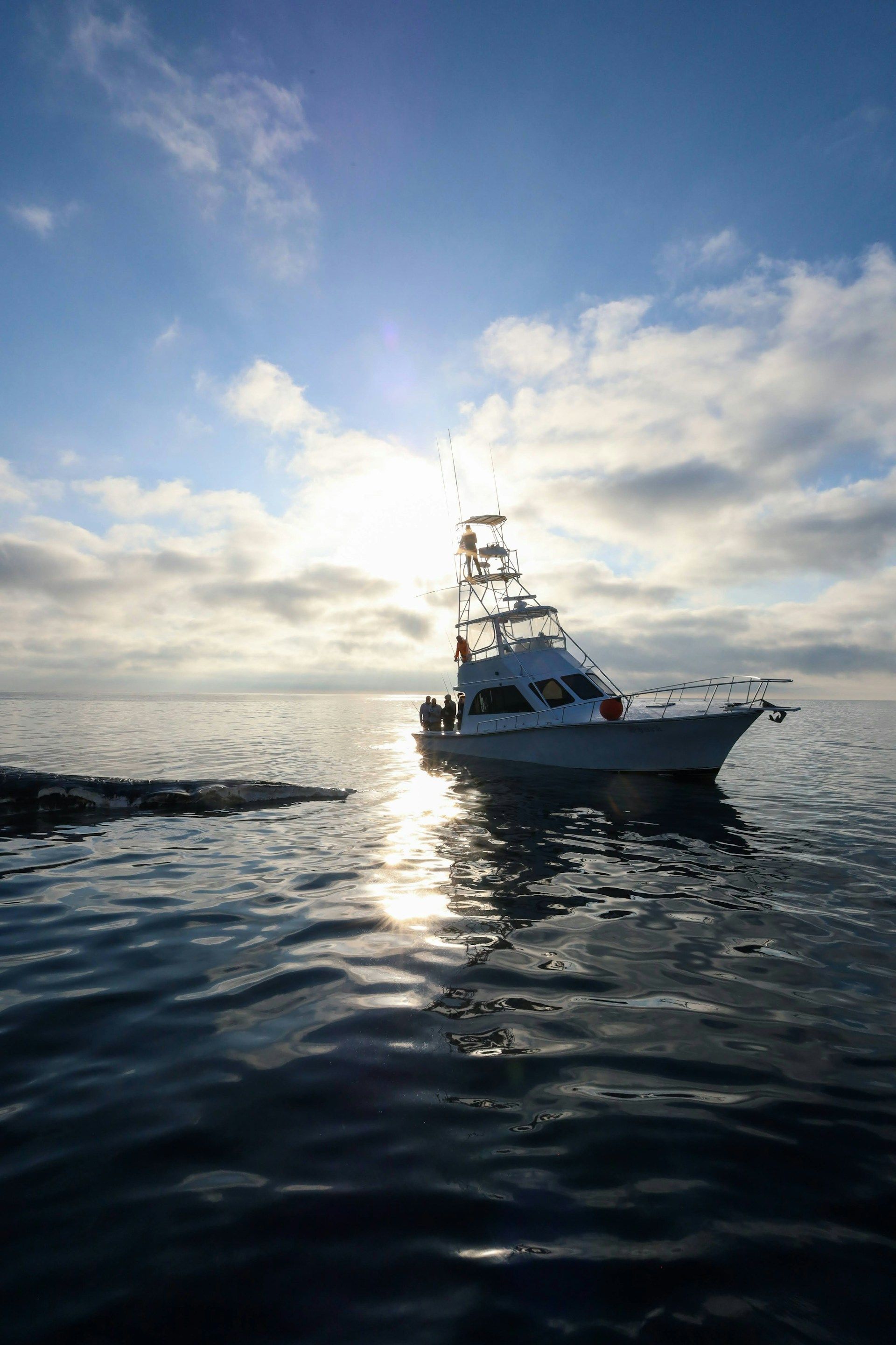 Boat on calm water at sunset, silhouetted against a bright sky with clouds and sun glare