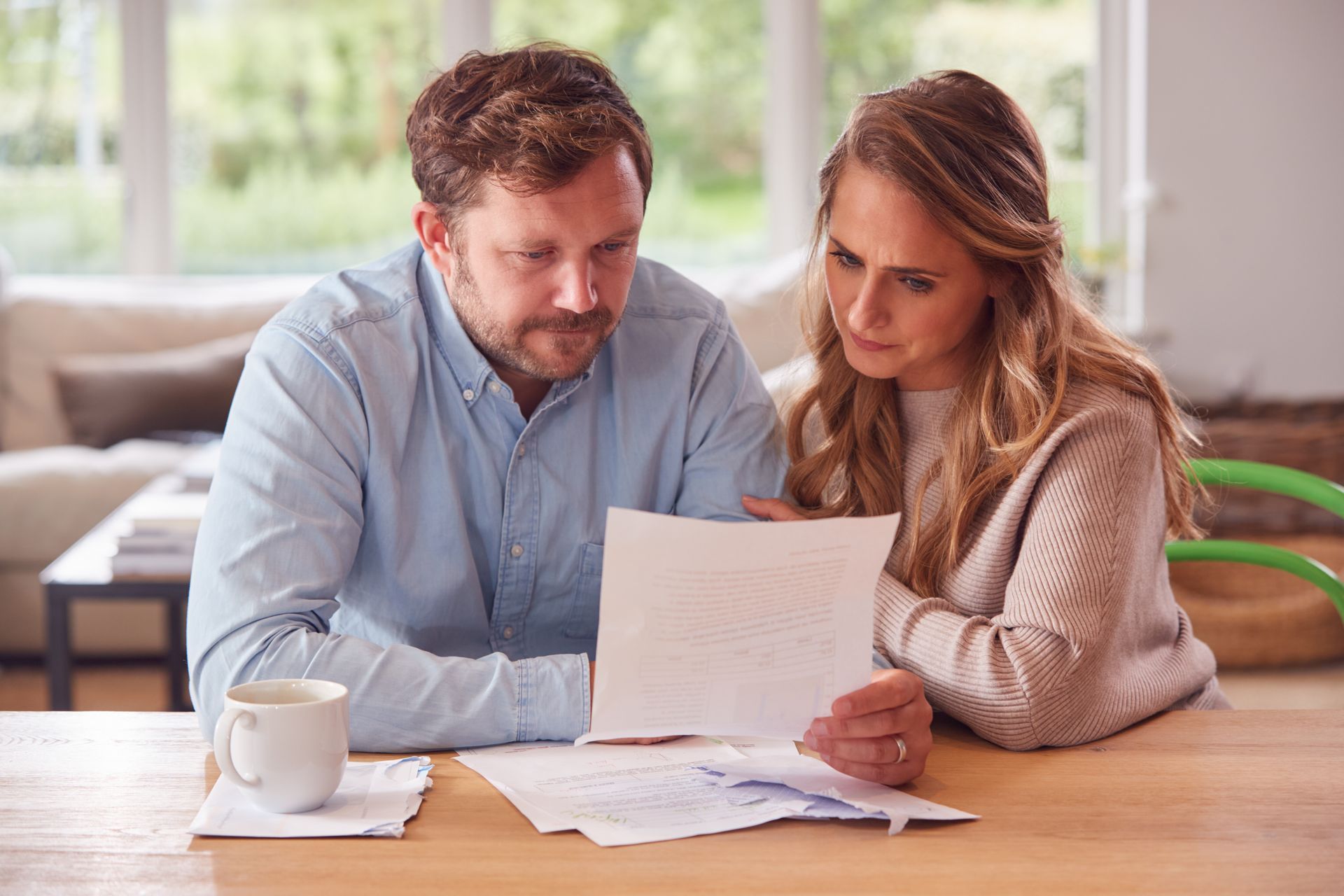 Two people review documents at a wooden table in a bright living room.