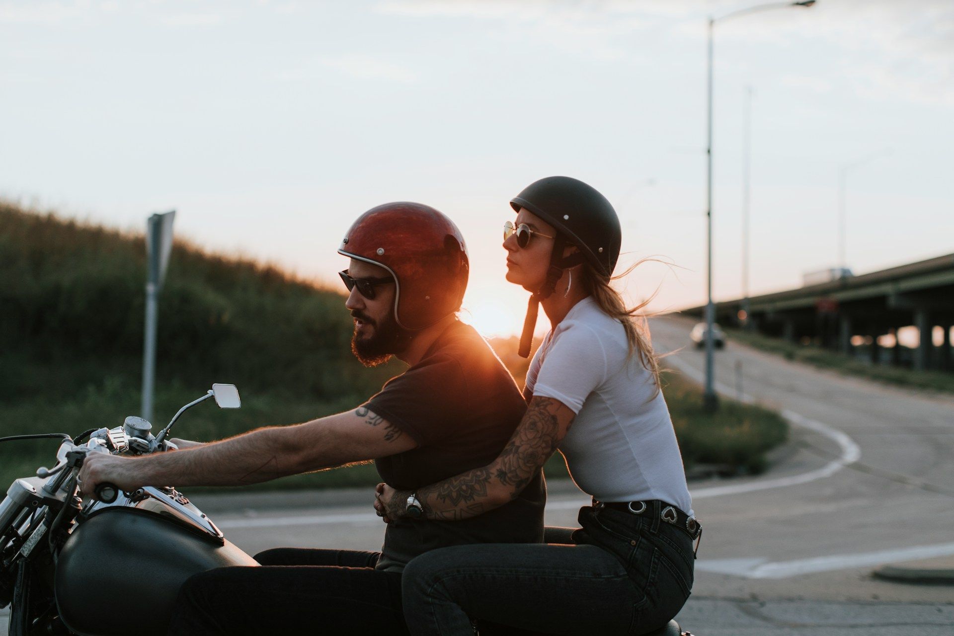 Two people ride a motorcycle on a curving road at sunset